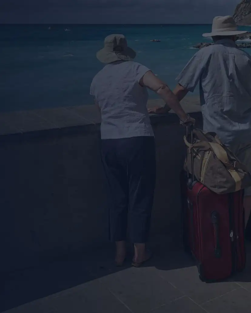 Pareja de adultos mayores con su equipaje frente al mar