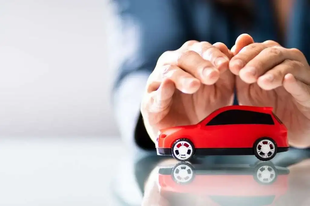 Manos que protegen un coche rojo de juguete